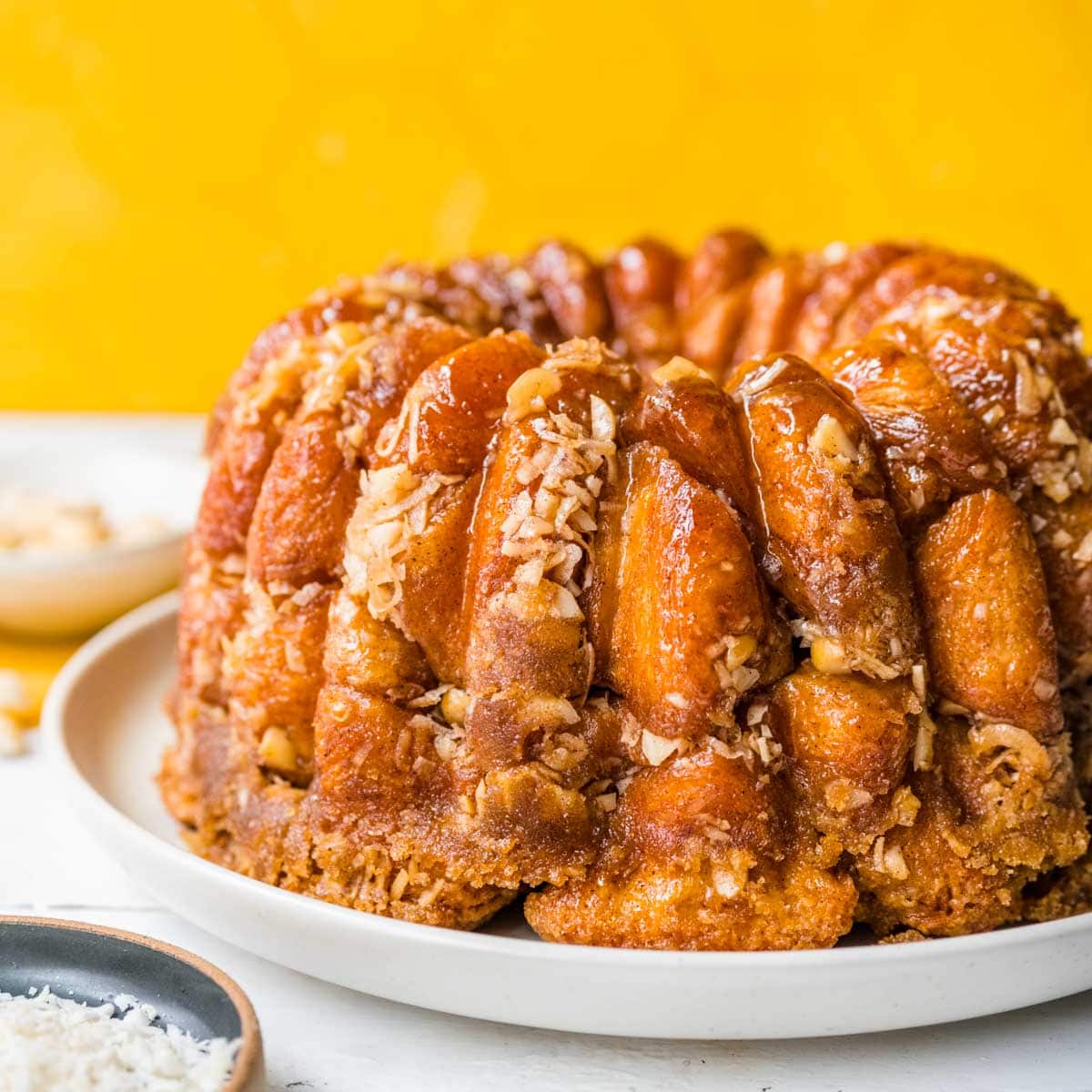 Hawaiian Monkey Bread finished on plate with coconut shreds and macadamia nuts in small bowls next to plate