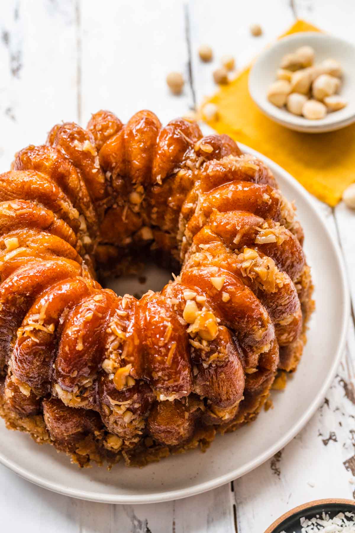 Hawaiian Monkey Bread finished on plate with coconut shreds and macadamia nuts in small bowls next to plate, top down view