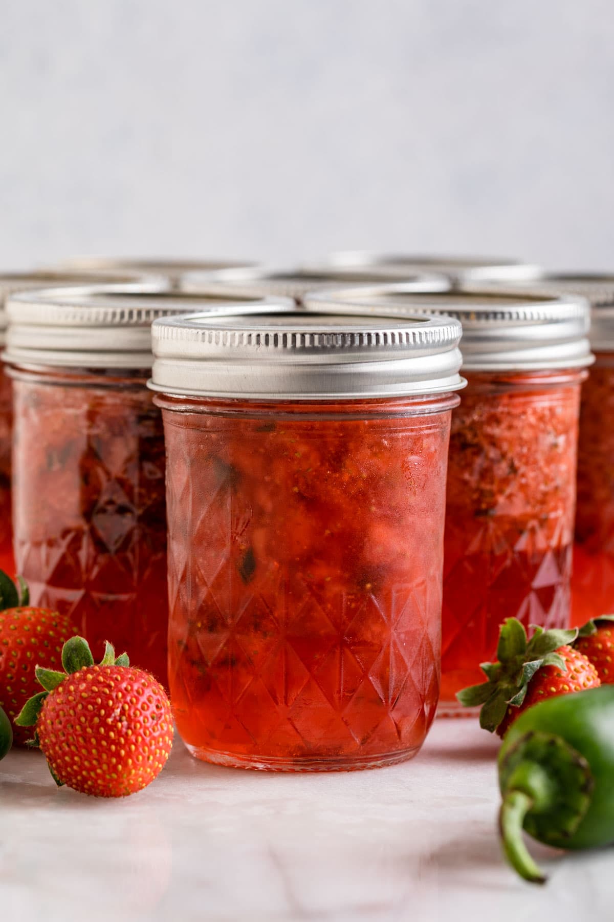Strawberry Jalapeno Jam in jars with fresh strawberry and jalapeno around jars