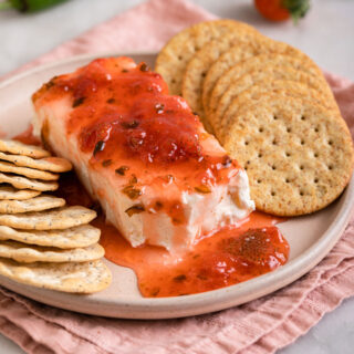Strawberry Jalapeno Jam poured on block of cream cheese with round crackers on plate