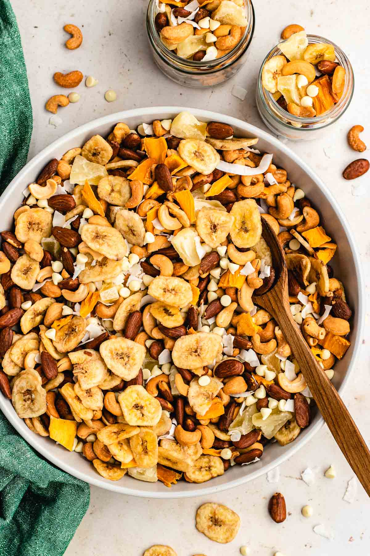Tropical Trail Mix combined in large bowl with wooden spoon and two jars filled with mix, top down view