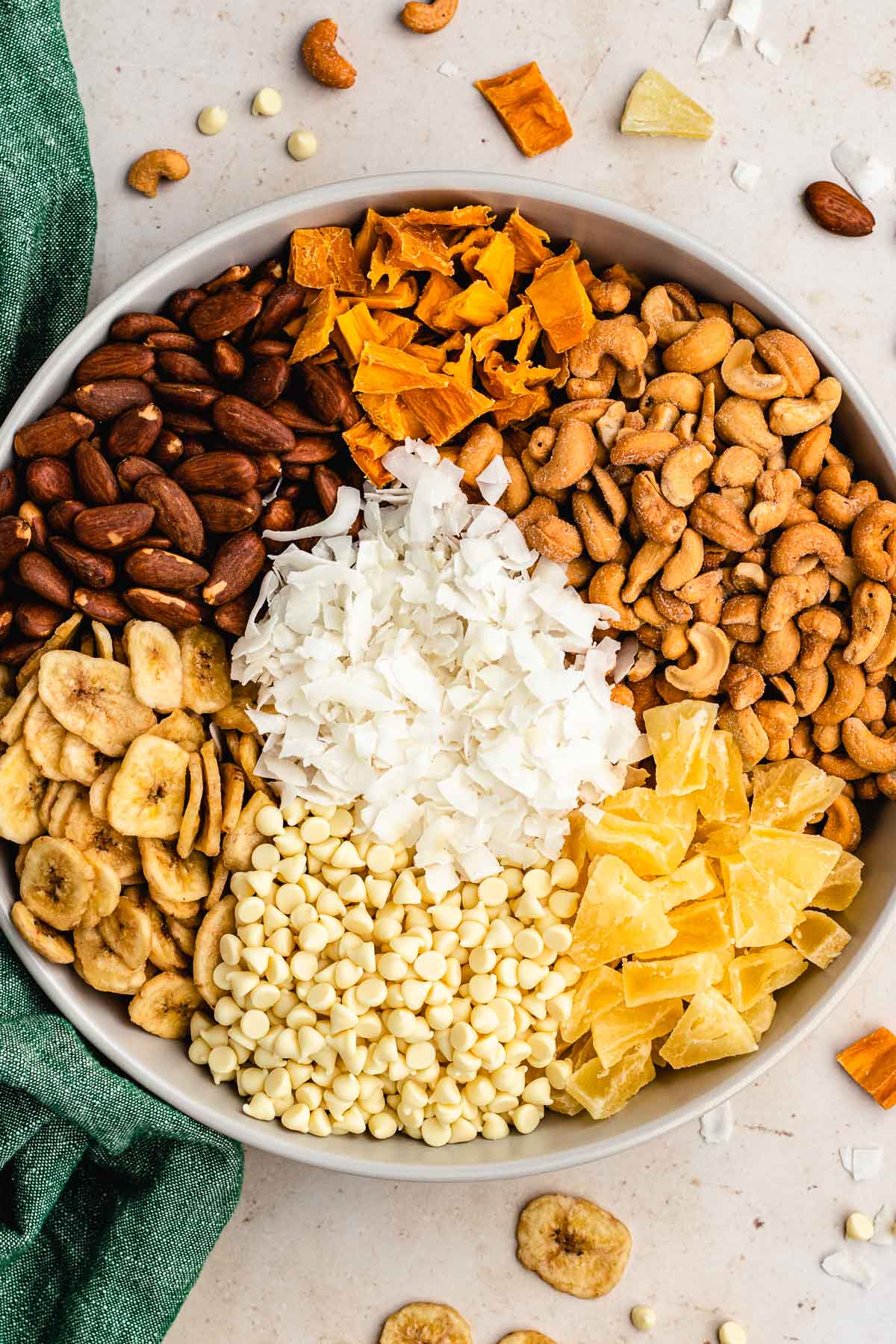 Tropical Trail Mix ingredients segmented in bowl with mango at top then cashews, pineapple, white chocolate, banana chips, almonds with coconut in center