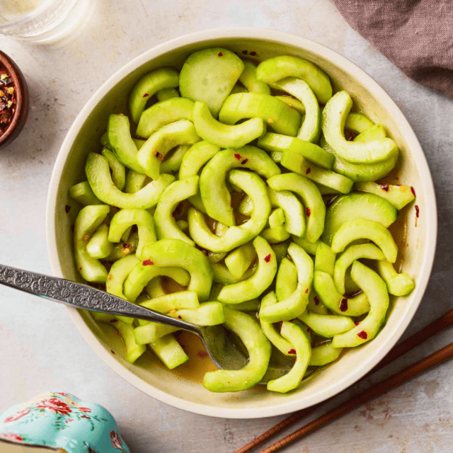 crunchy green veggies mixed with dressing in a white bowl and a spoon