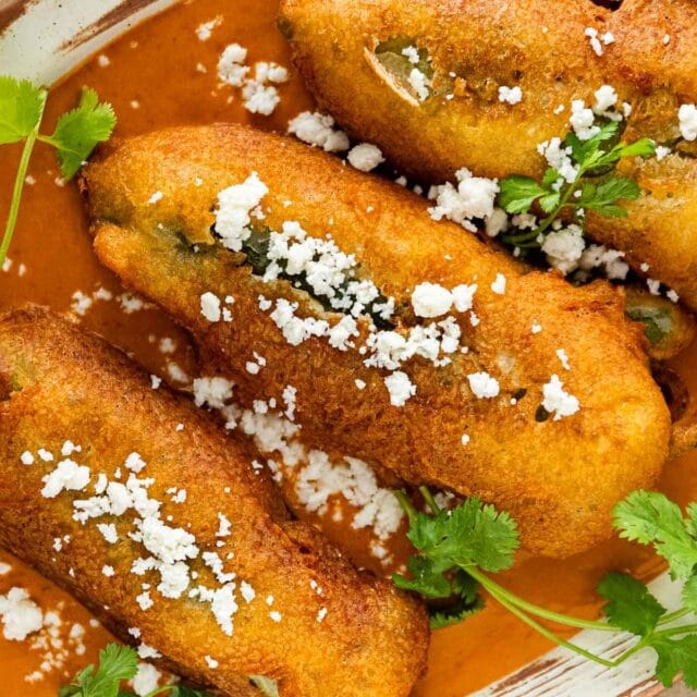 Fried stuffed chilies on a white plate with red sauce