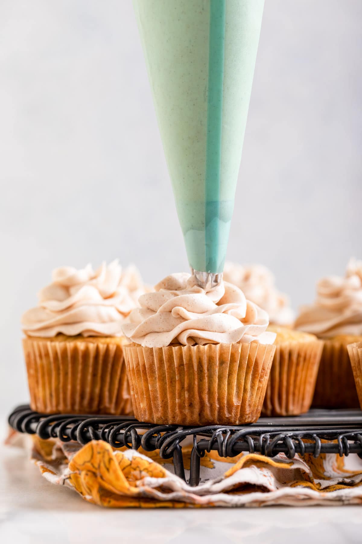 Banana Cupcakes piping frosting on cupcakes on cooling rack,