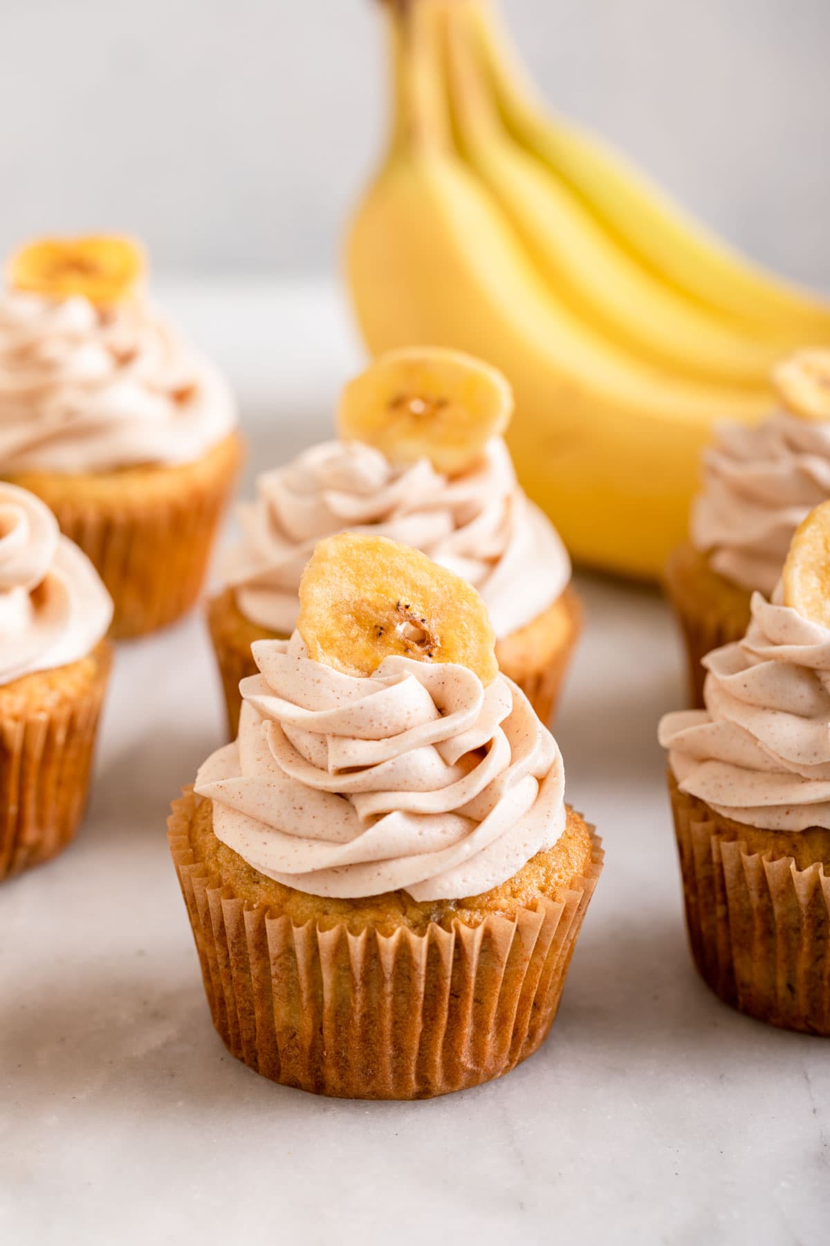 Banana Cupcakes frosted and lined up on white background with bananas bunch behind them