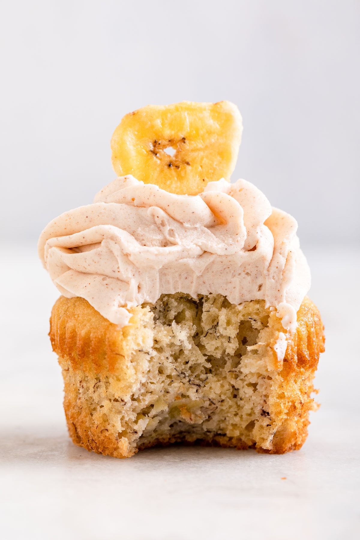 Banana Cupcake frosted and decorated with banana chip with bite taken out of it.