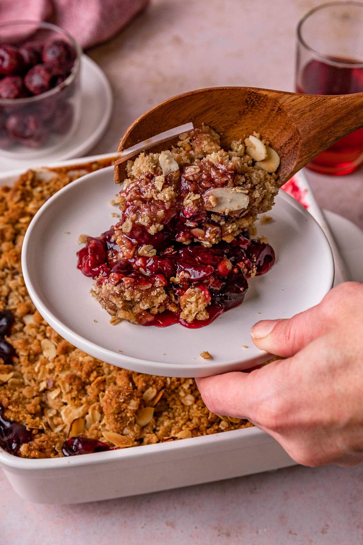 Cherry Crisp prepared in baking dish and scooping out portion onto plate with wooden spoon