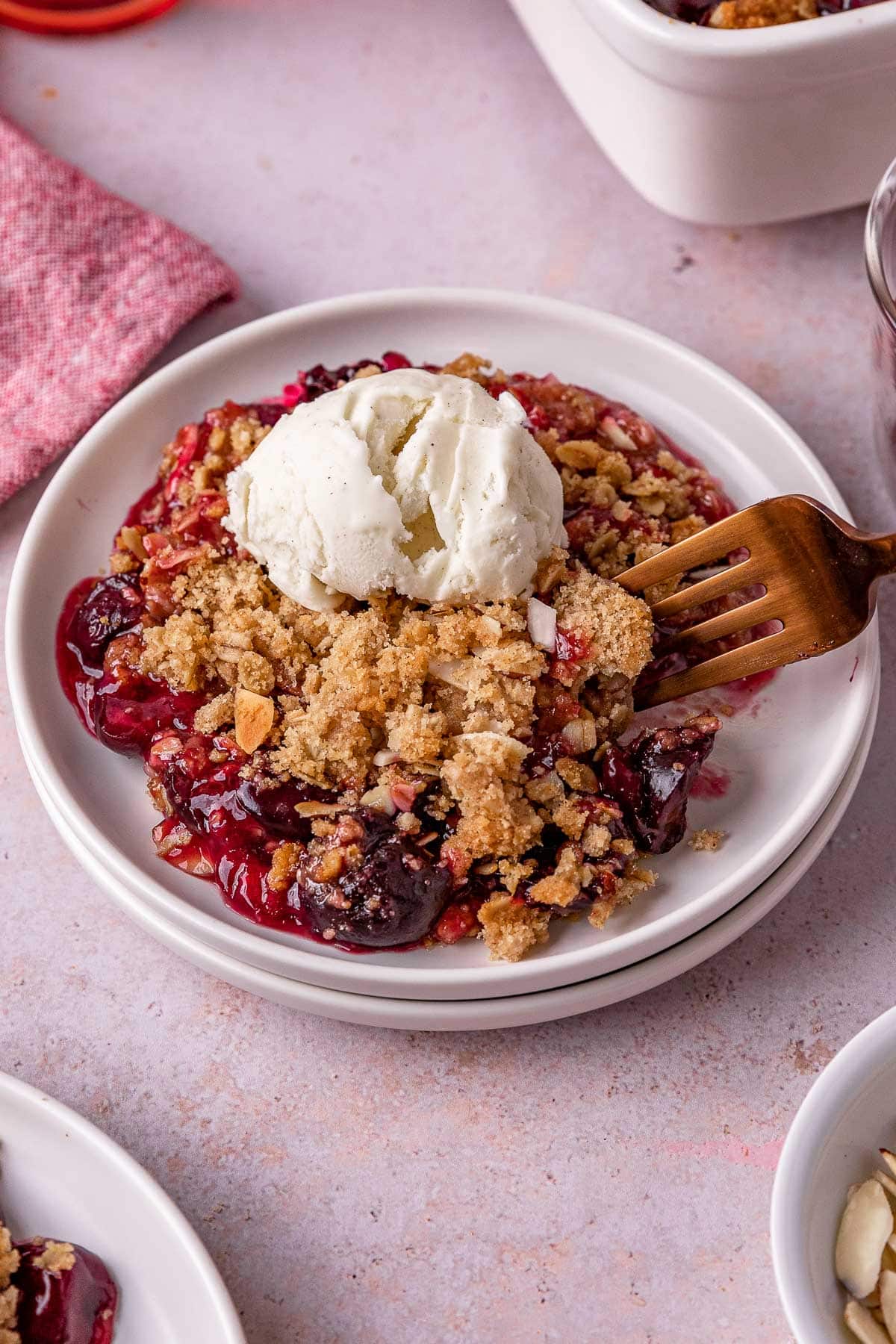 Cherry Crisp prepared and plated with scoop of vanilla ice cream on top with fork taking portion