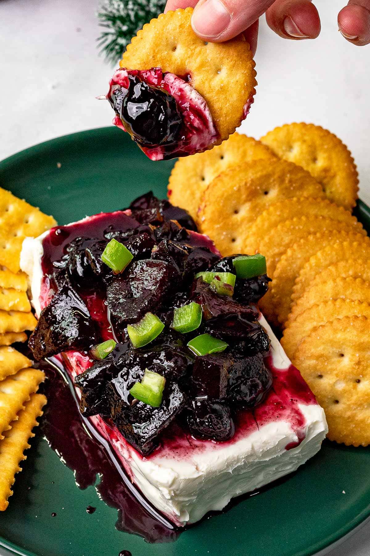 Cherry Jalapeno Jam prepared and served on cream cheese with crackers, dipping cracker in jam and cream cheese