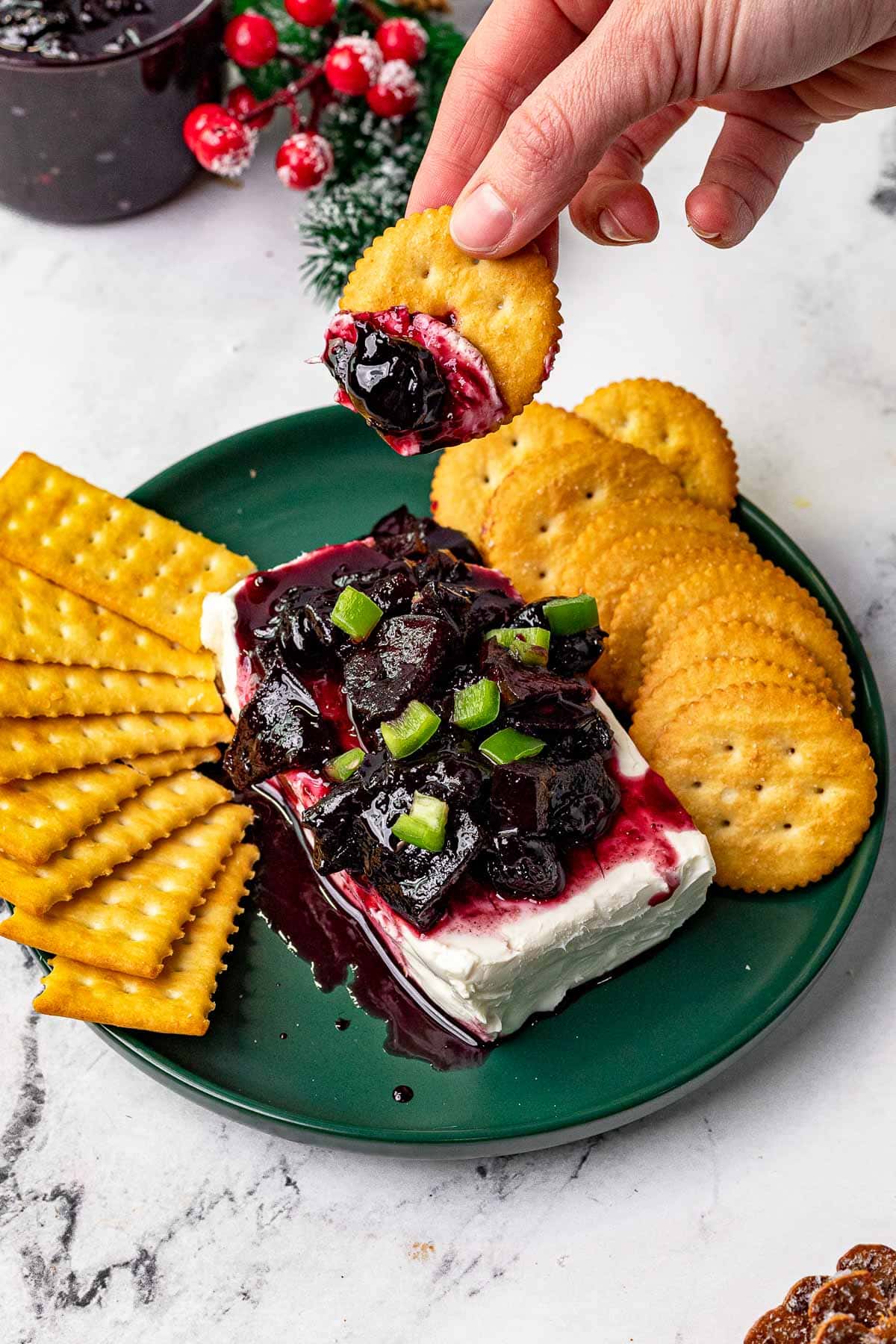 Cherry Jalapeno Jam prepared and served on cream cheese with crackers, dipping cracker in jam and cream cheese