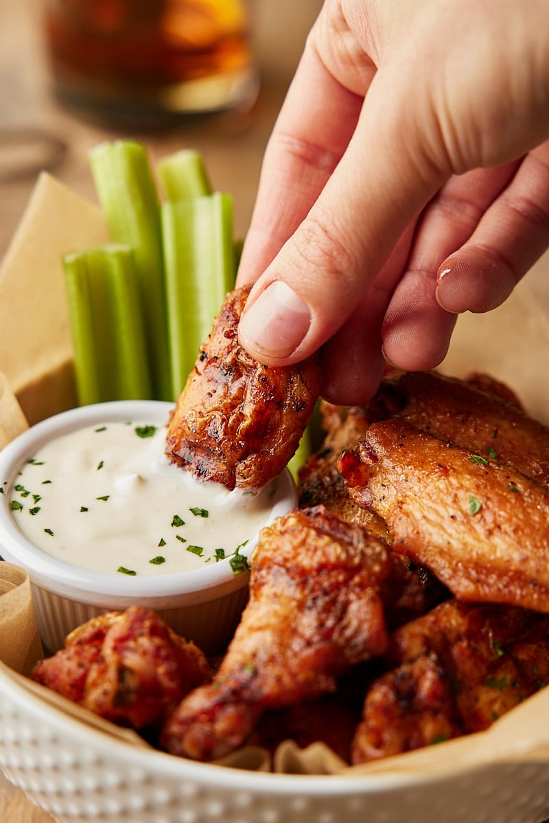 Grilled Chicken Wings cooked in a basket with hand dipping wing into ranch sauce and celery sticks