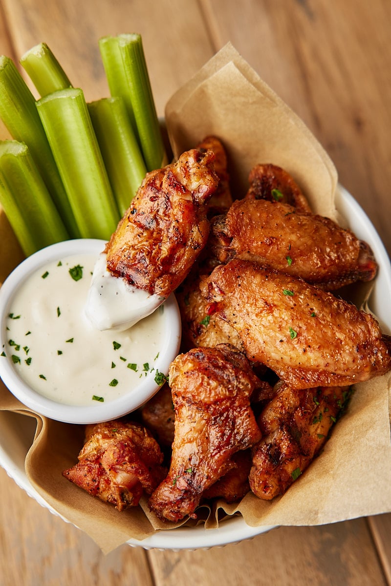 Grilled Chicken Wings cooked in a basket with one wing resting on dipping sauce and celery sticks