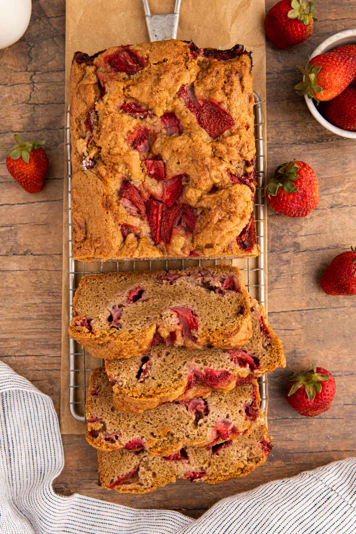 Strawberry Bread loaf half sliced and half whole on wire rack with berries scattered around