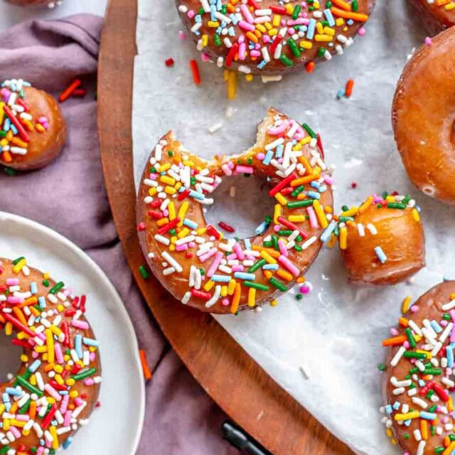 Donuts with sprinkles, one has a bite out of it.