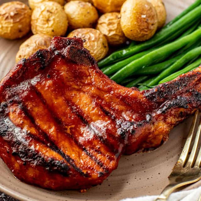 Cooked pork chop on dinner plate with green beans and potatoes.