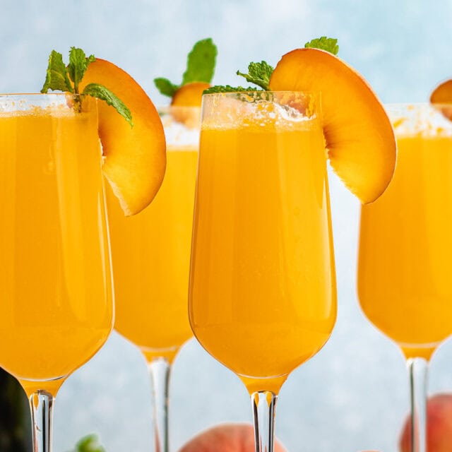 Finished cocktails in champagne glasses with peach and mint garnish