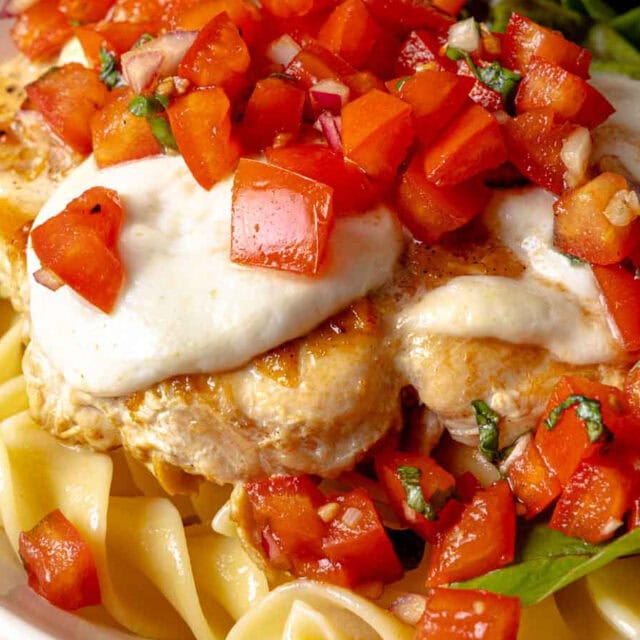 Chicken breast on pasta, topped with mozzarella and tomato.