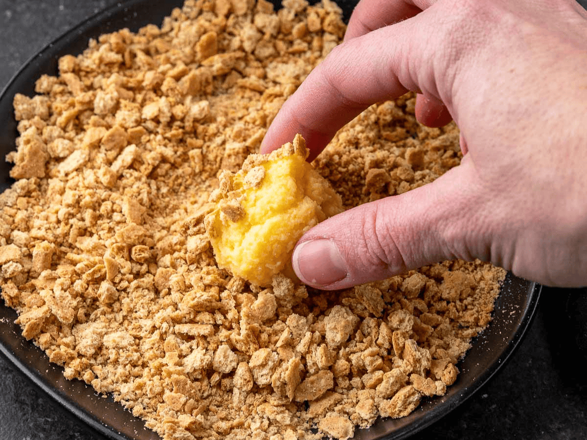 Cake ball being dipped in graham cracker crumbs.
