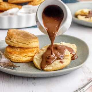 Chocolate gravy being poured over biscuit on plate.