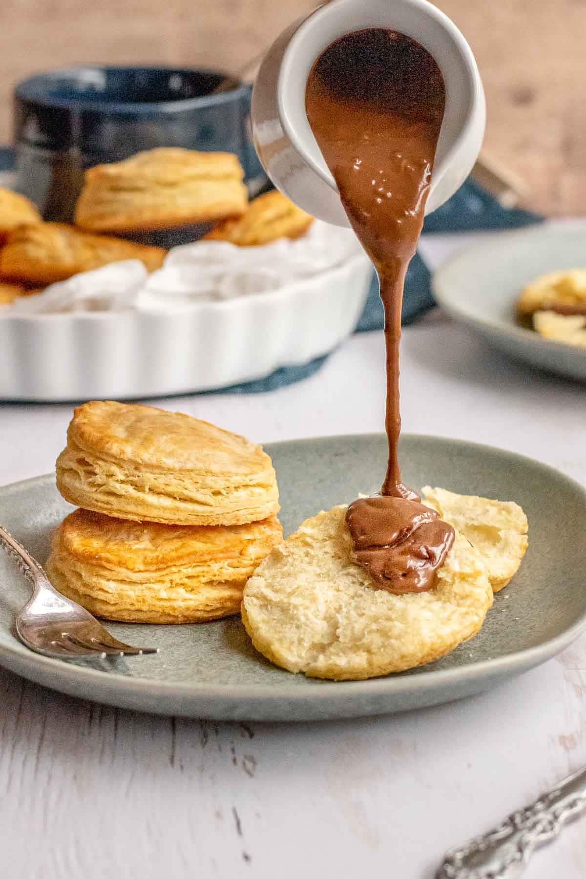 Chocolate gravy being poured over biscuit on plate.