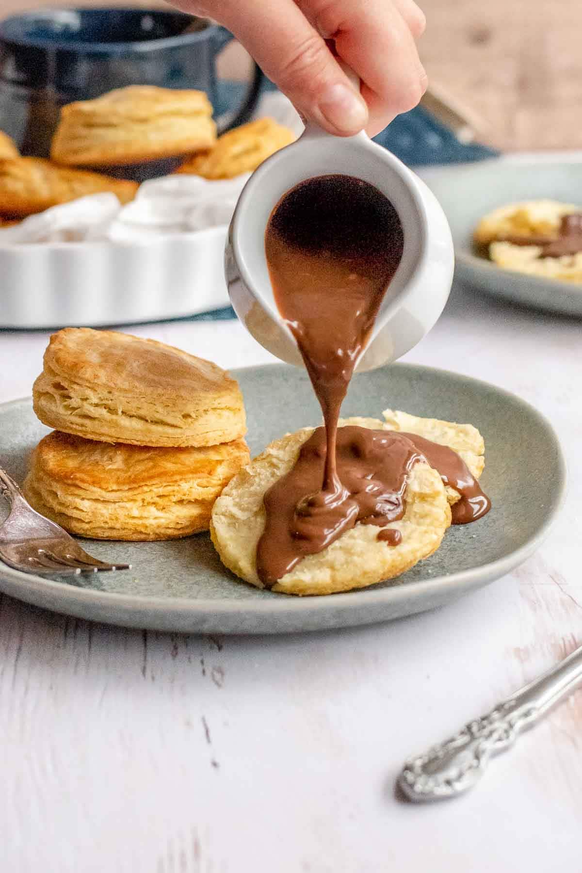 Chocolate gravy being poured over biscuits, on plate.