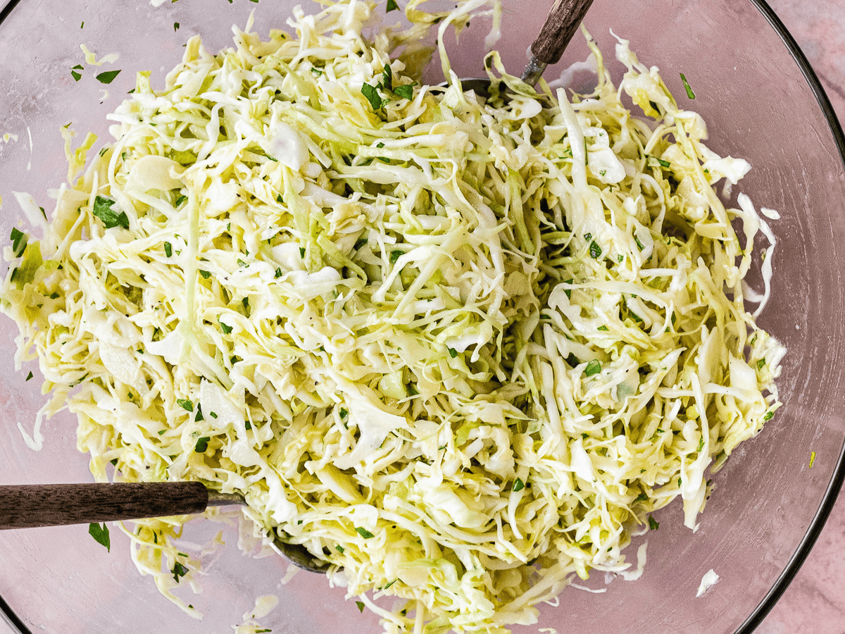 Shredded salad being tossed in bowl.