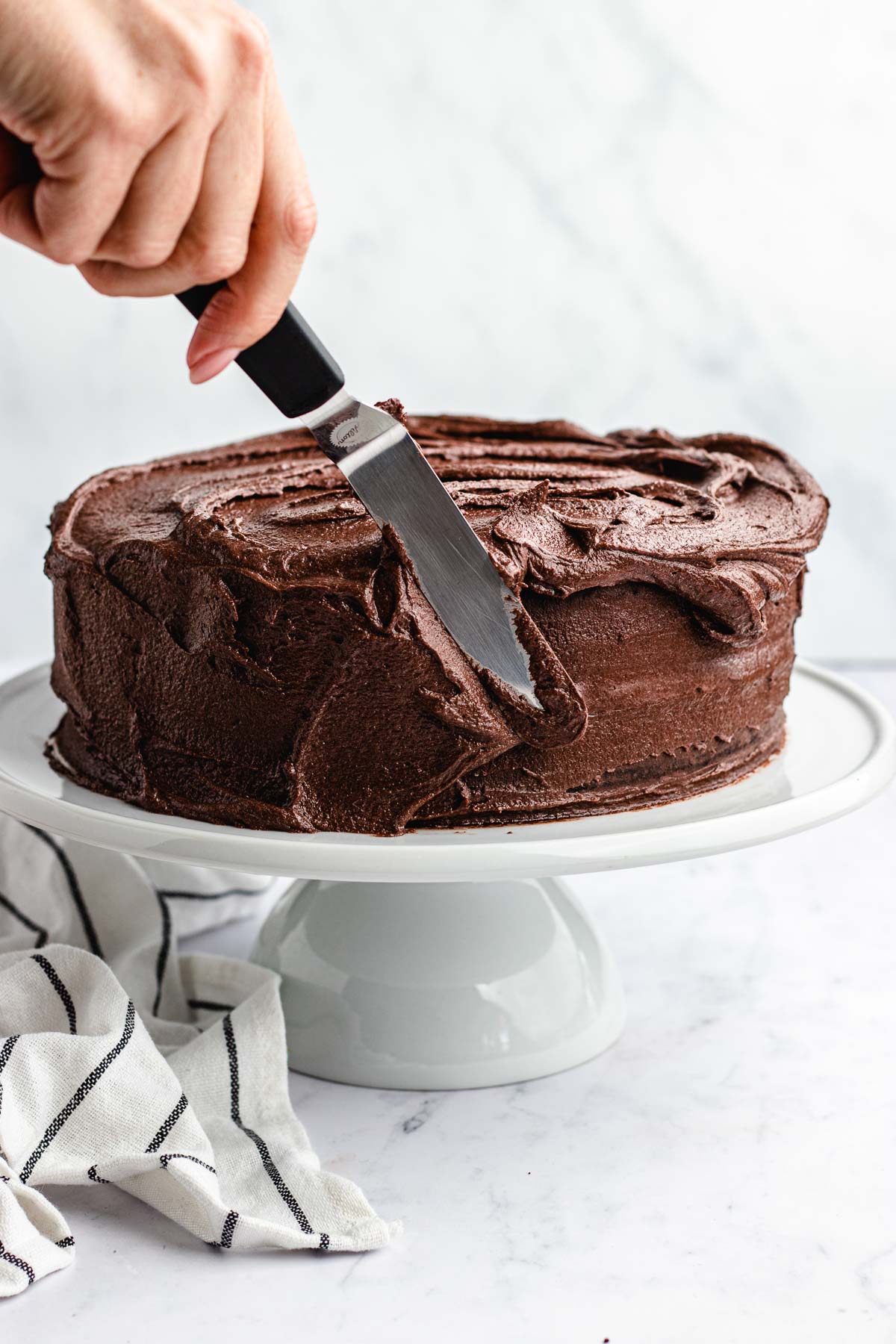 Dark Chocolate Frosting spreading on layer cake on white cake stand