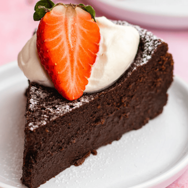 Slice of cake with powdered sugar, dollop of whipped cream and a strawberry cut in half