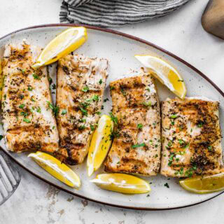 Grilled mahi mahi on serving plate with lemon wedges.