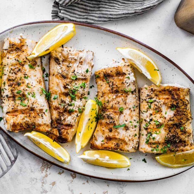 Grilled mahi mahi on serving plate with lemon wedges.