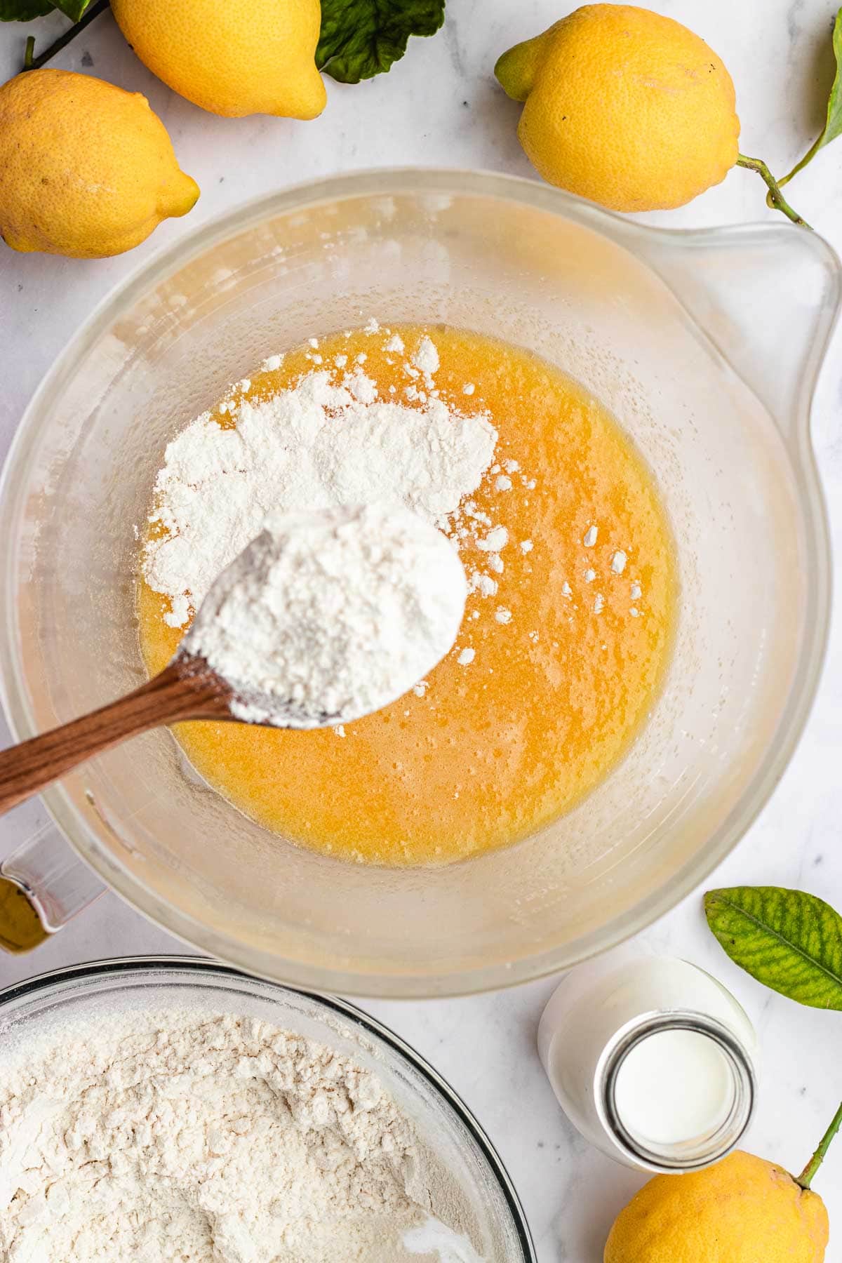 Lemon Olive Oil Cake adding flour to mixed wet ingredients with a spoon.