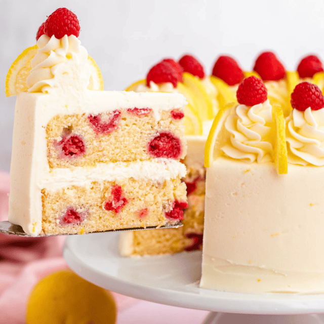 Slice of dessert being removed from the whole, with white frosting and red and yellow fruit on top and within the dessert