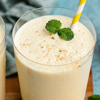 Glass of mango lassi with mint garnish and straw.