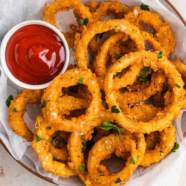 Onion rings on serving plate with ketchup.