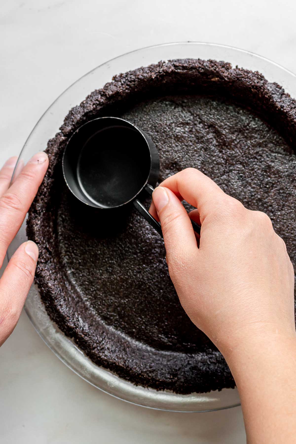 Oreo Coffee Ice Cream Pie pressing cookie crumbs in pie plate with measuring cup