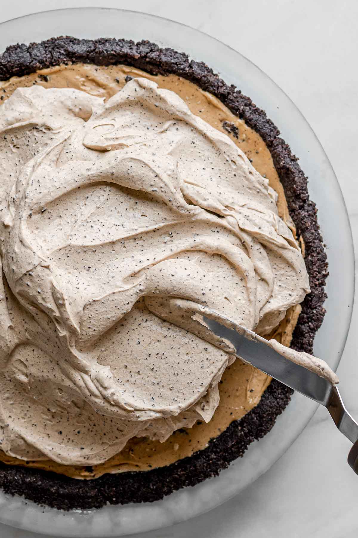 Oreo Coffee Ice Cream Pie spreading whipped topping on ice cream layer in crust