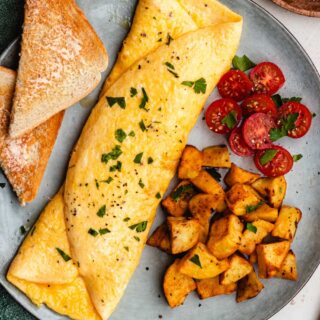 Omelette on plate with toast, potatoes, and tomatoes.