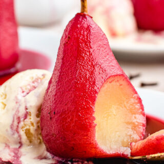Pear with bite and red wine reduction on a plate with vanilla ice cream.