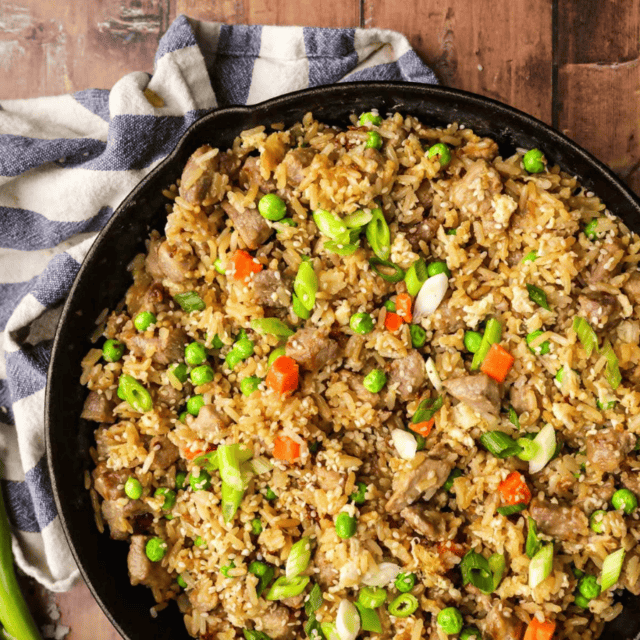 Skillet of fried rice on brown table with grey and white rag