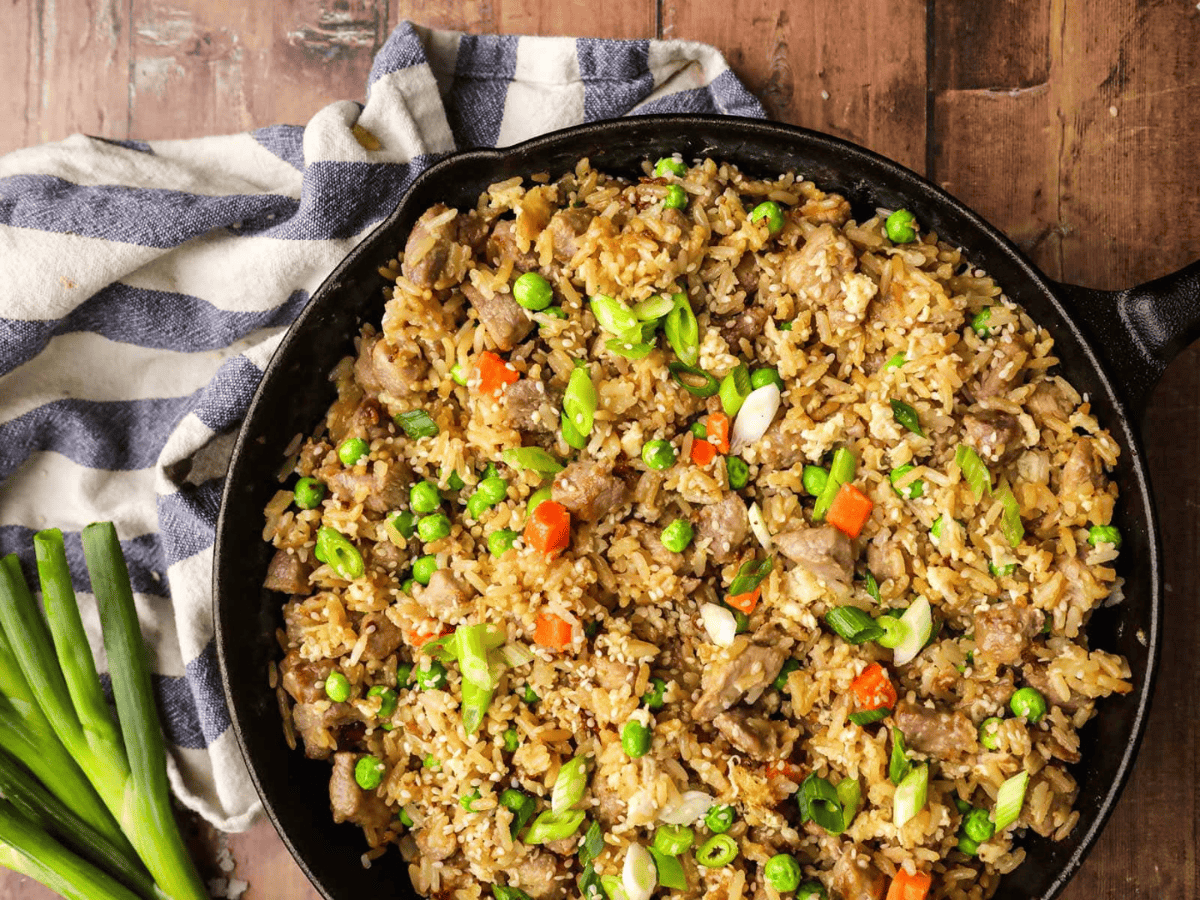 Skillet of fried rice on brown table with grey and white rag