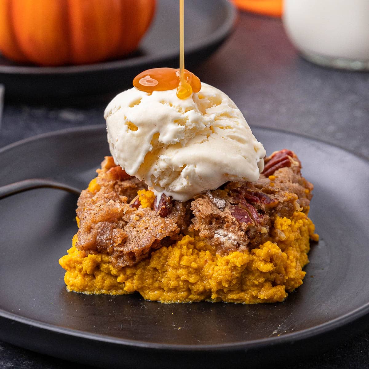 One slice of Pumpkin Dump Cake on a black plate with a single scoop of vanilla ice cream and caramel drizzle.