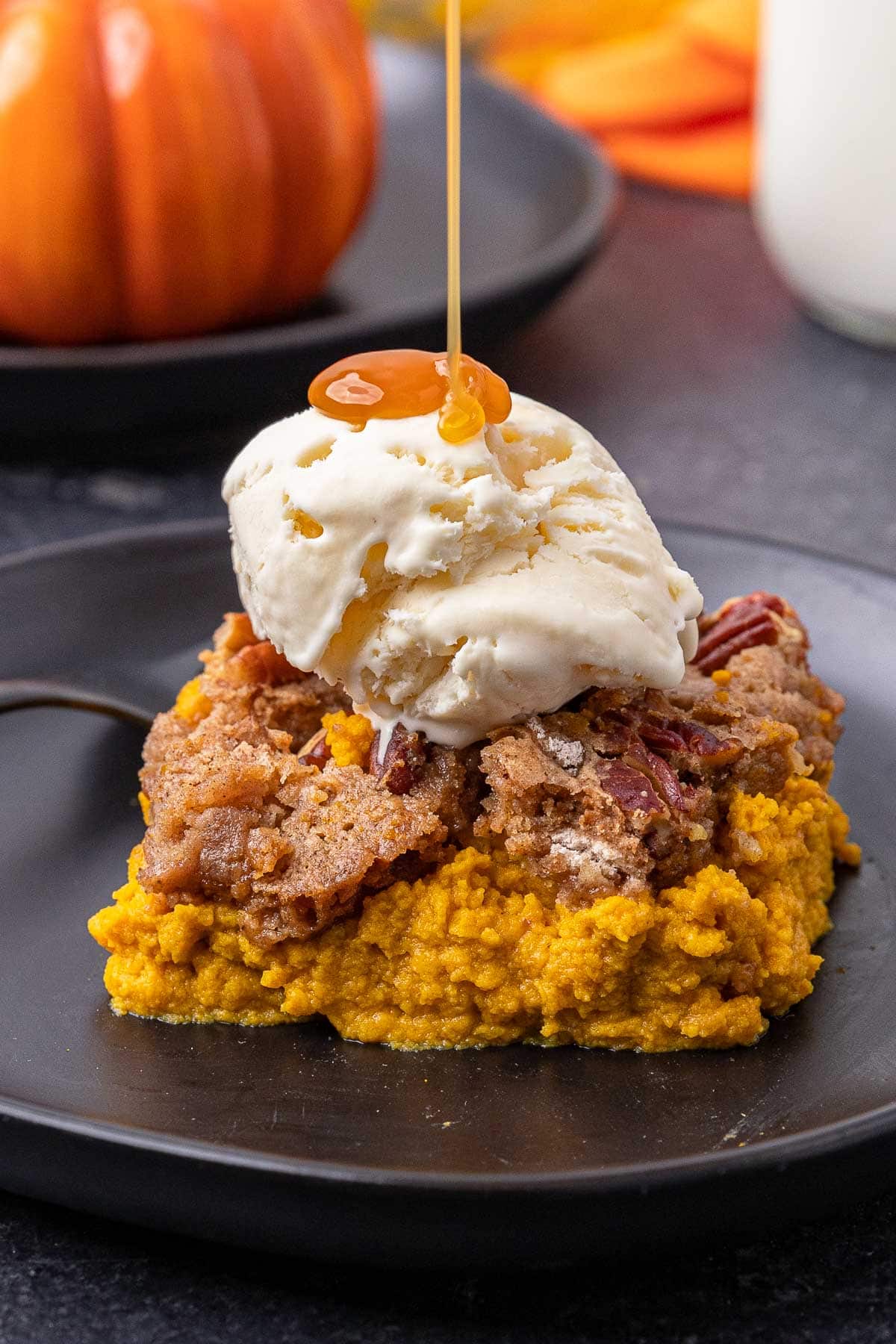 Pumpkin Dump Cake slice on a plate with a scoop of vanilla ice cream on top and caramel drizzle.