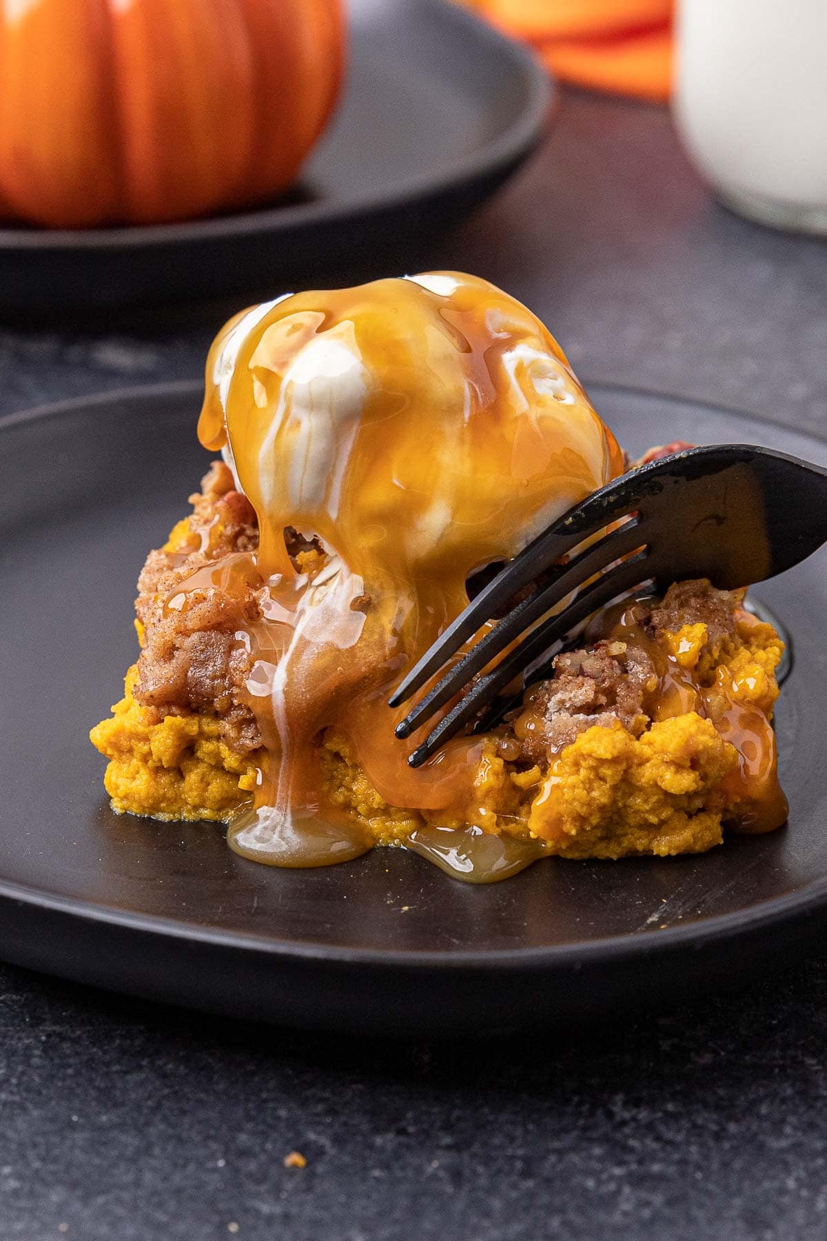 Pumpkin Dump Cake slice on a black plate with a scoop of vanilla ice cream and caramel on top.