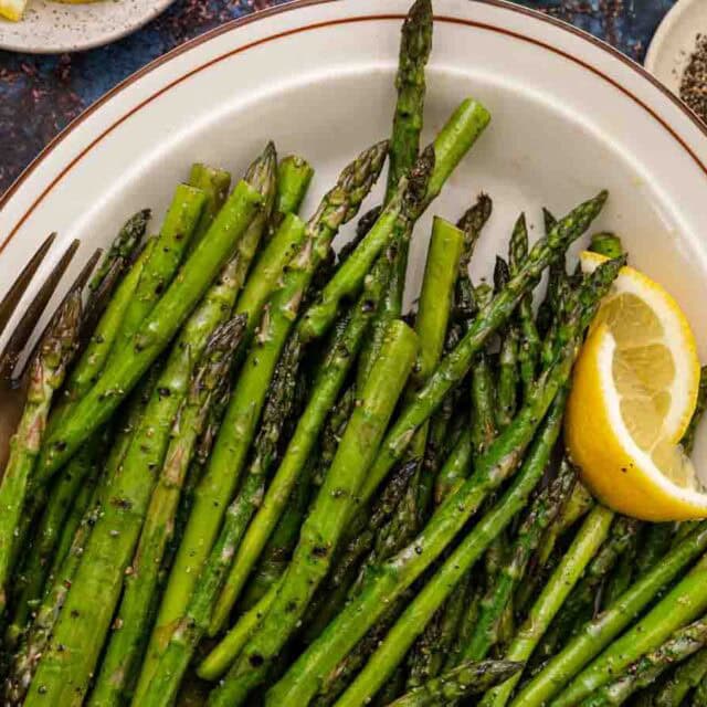 Asparagus on serving plate with lemon wedges.