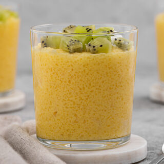 Pudding topped with kiwi cubes, in a clear glass dessert cup.