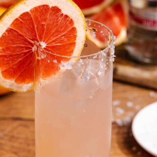 Cocktail in glass with salted rim and grapefruit wheel garnish.