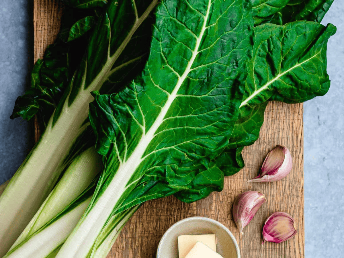 Whole leaves of chard on cutting board with garlic cloves.