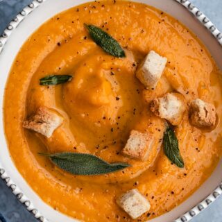 Bowl of creamy soup with croutons and fresh sage.