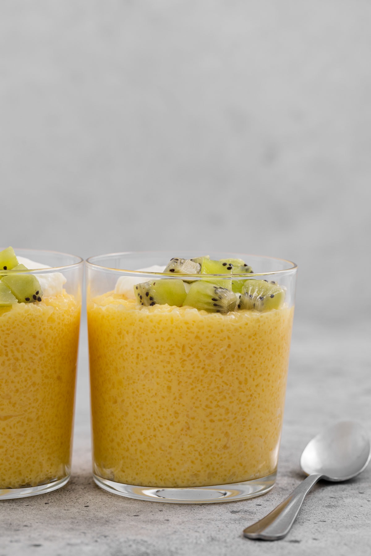 Two dessert glass cups filled with tapioca and topped with cubed kiwi.